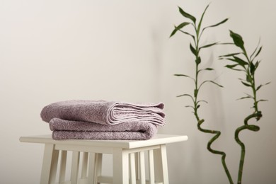 Photo of Violet towels on stool against white wall. Space for text
