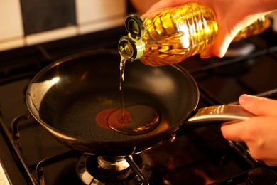 Photo of Vegetable fats. Woman pouring oil into frying pan on stove, closeup