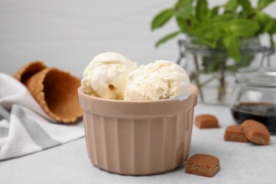 Scoops of ice cream with caramel sauce and candies on light grey table, closeup