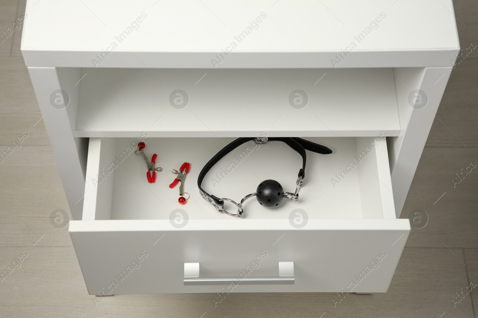 Photo of Black ball gag and nipple clamps in drawer indoors, above view. Sex toys