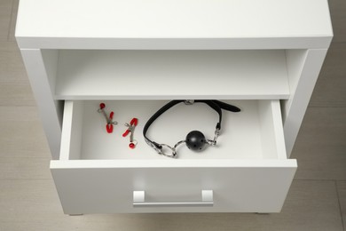 Photo of Black ball gag and nipple clamps in drawer indoors, above view. Sex toys