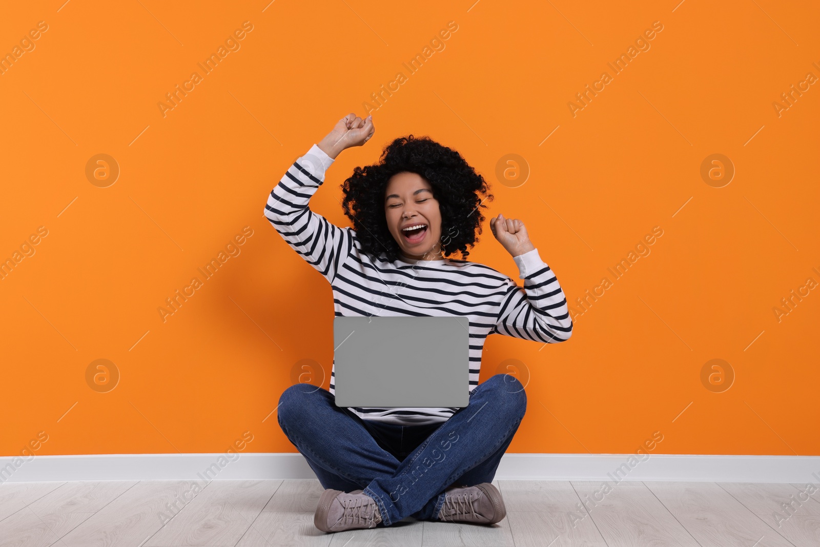 Photo of Emotional young woman with laptop near orange wall
