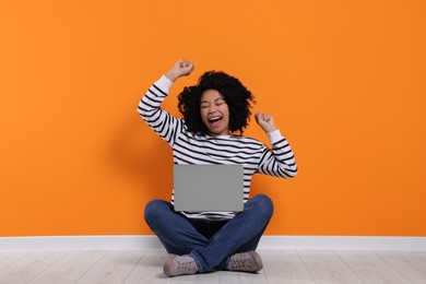 Emotional young woman with laptop near orange wall