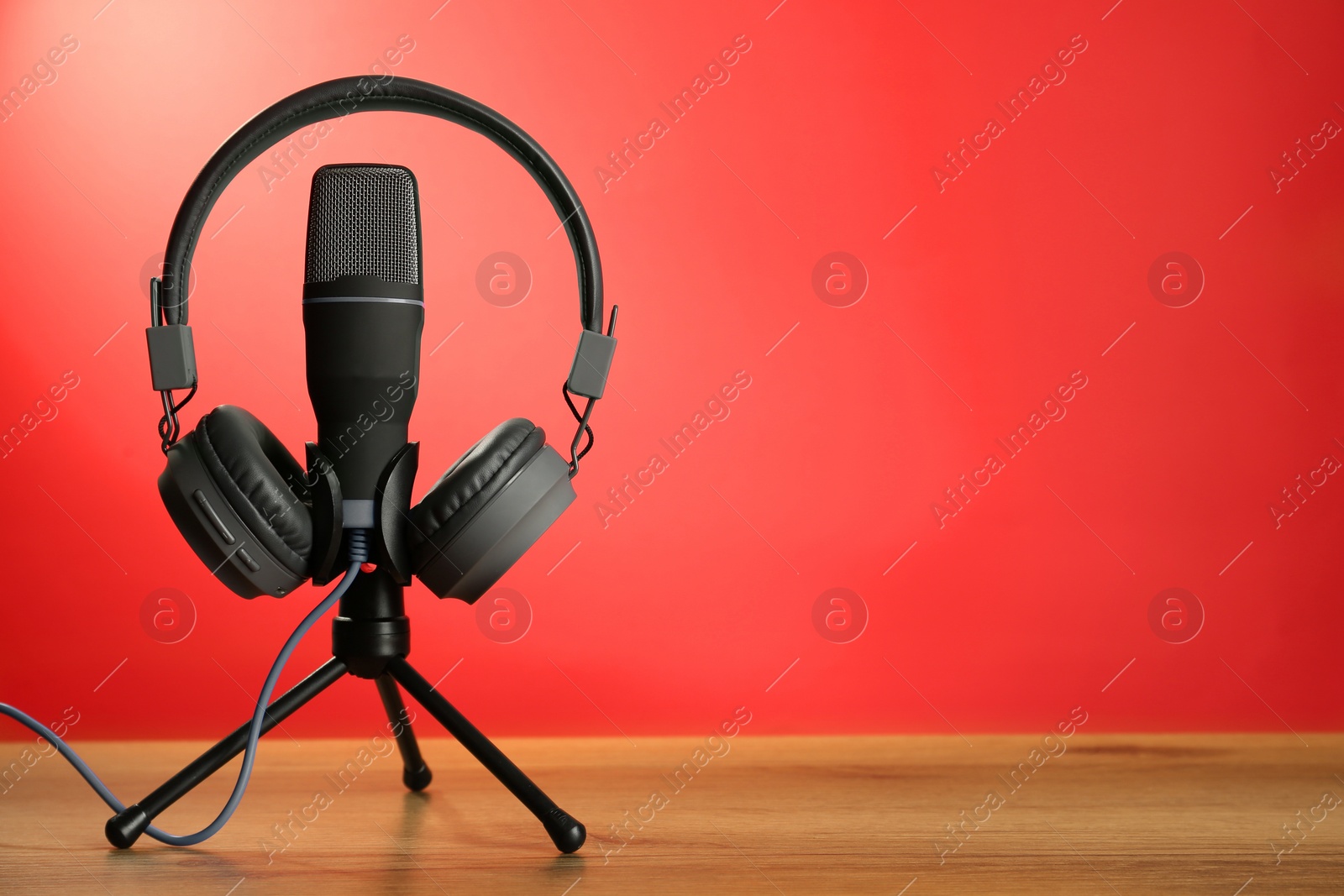 Photo of Microphone and modern headphones on wooden table against red background, space for text