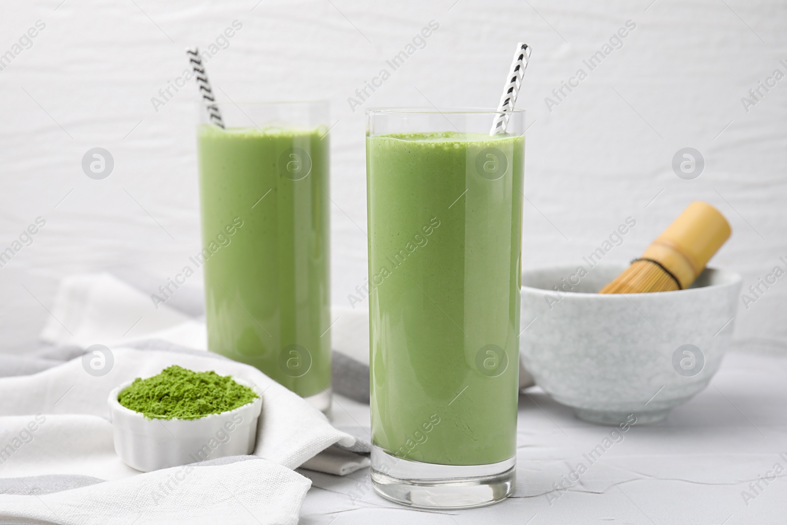 Photo of Glasses of tasty matcha smoothie and powder on white table