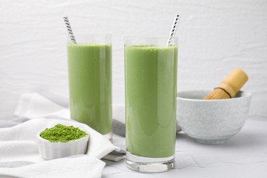 Glasses of tasty matcha smoothie and powder on white table