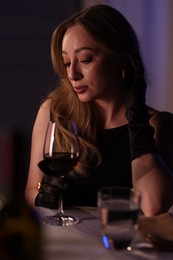 Elegant young woman with glass of wine at table indoors in evening