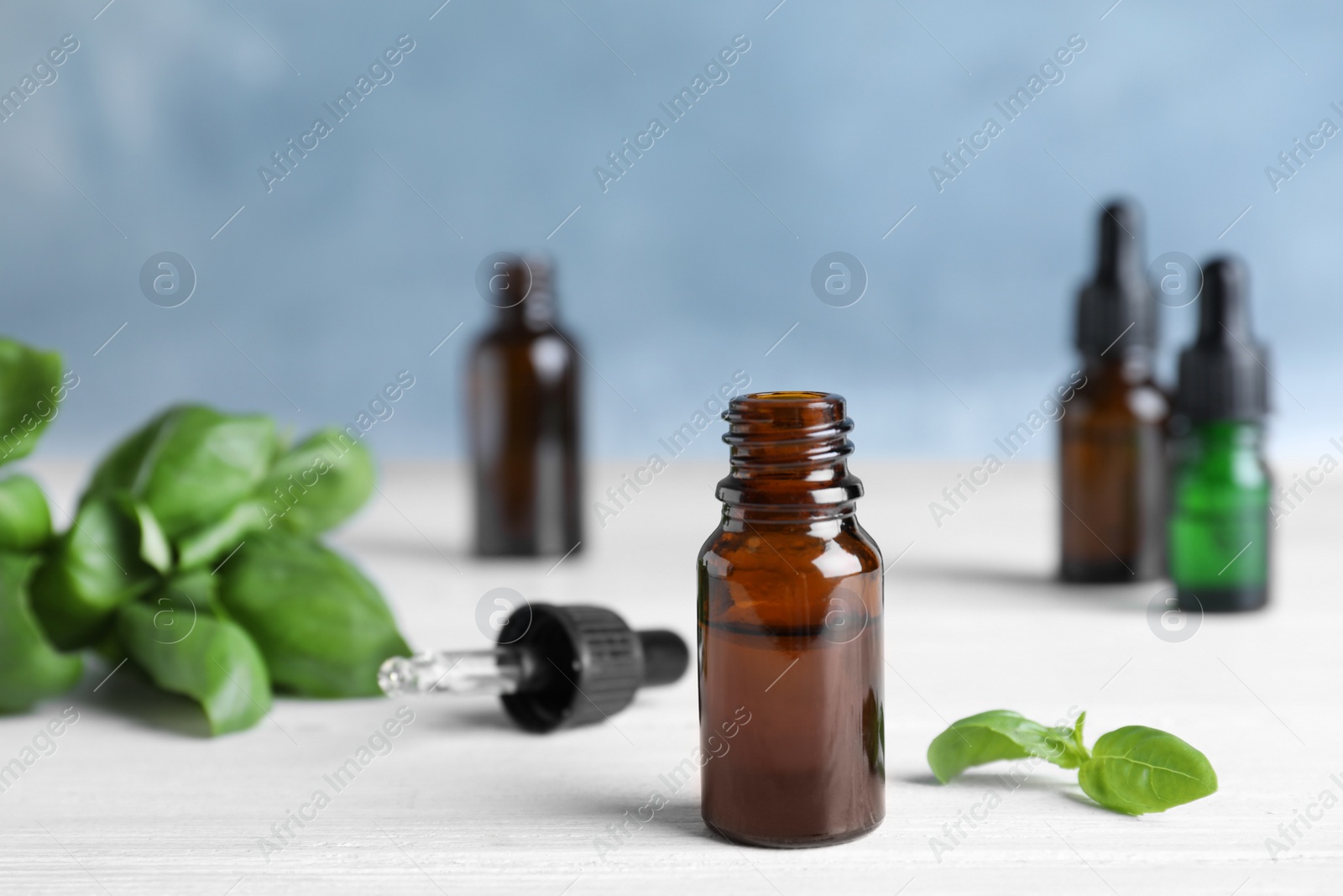 Photo of Glass bottle of essential oil, dropper and basil on table