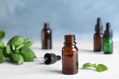 Photo of Glass bottle of essential oil, dropper and basil on table