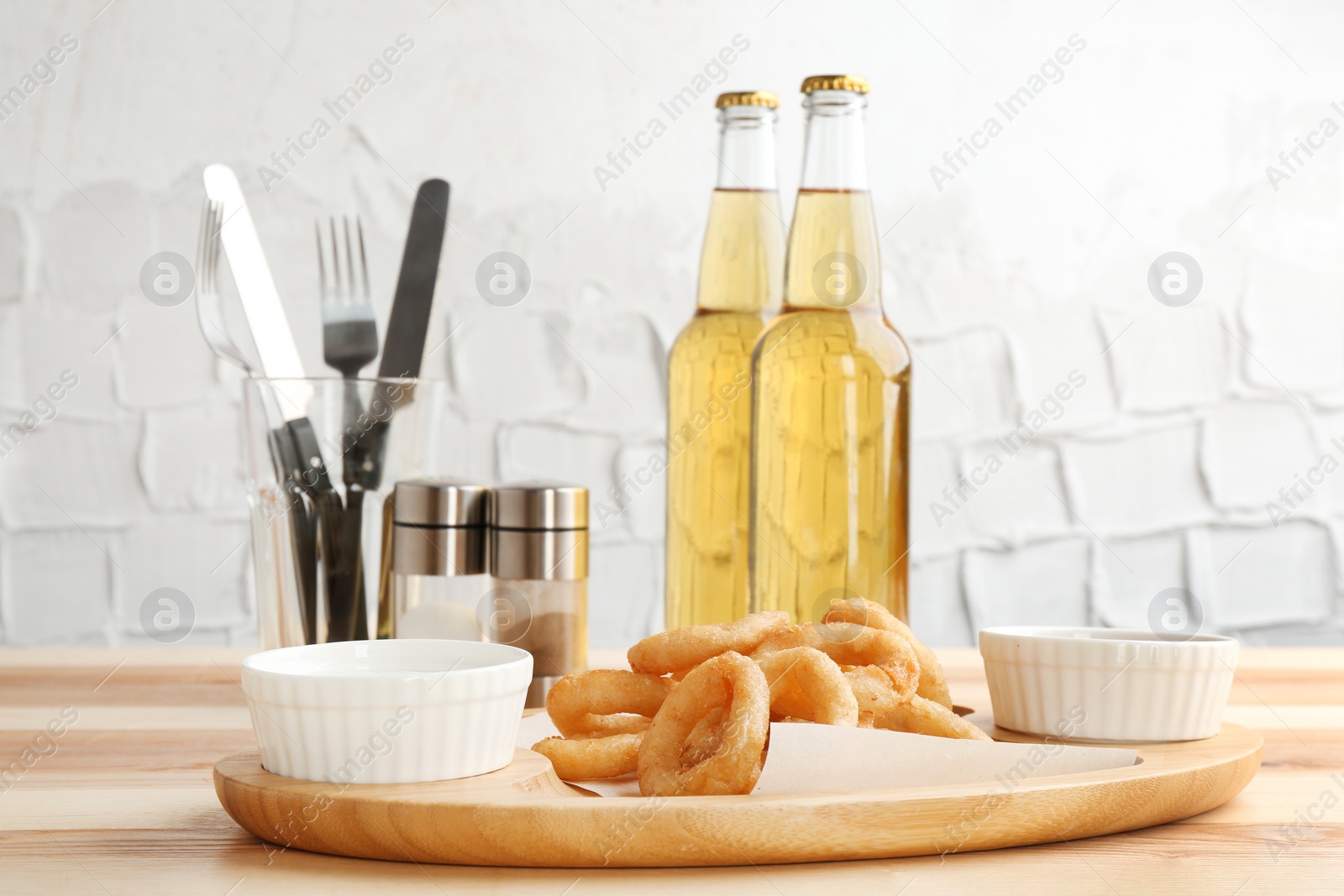 Photo of Tasty onion rings and bowls with sauces on wooden table