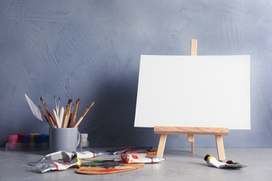 Easel with various artist tools on table against color wall. Space for text