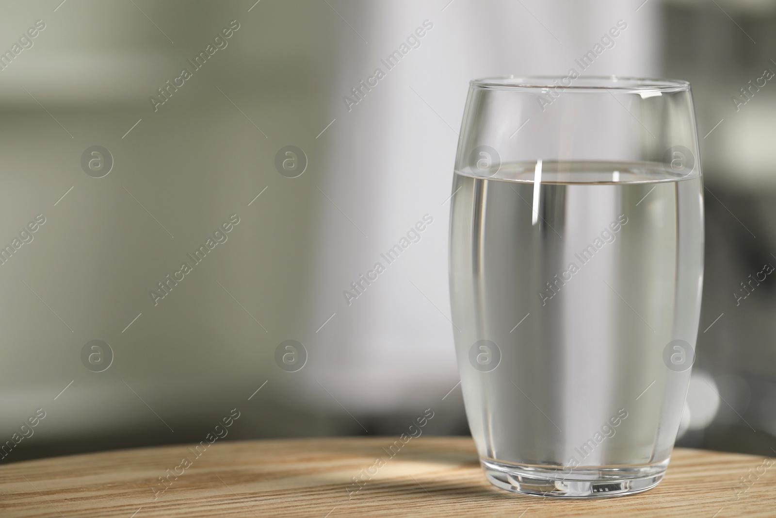 Photo of Glass of pure water on wooden table against blurred background, space for text
