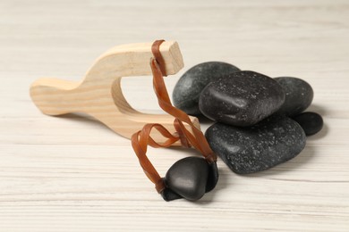 Slingshot with stones on white wooden table, closeup