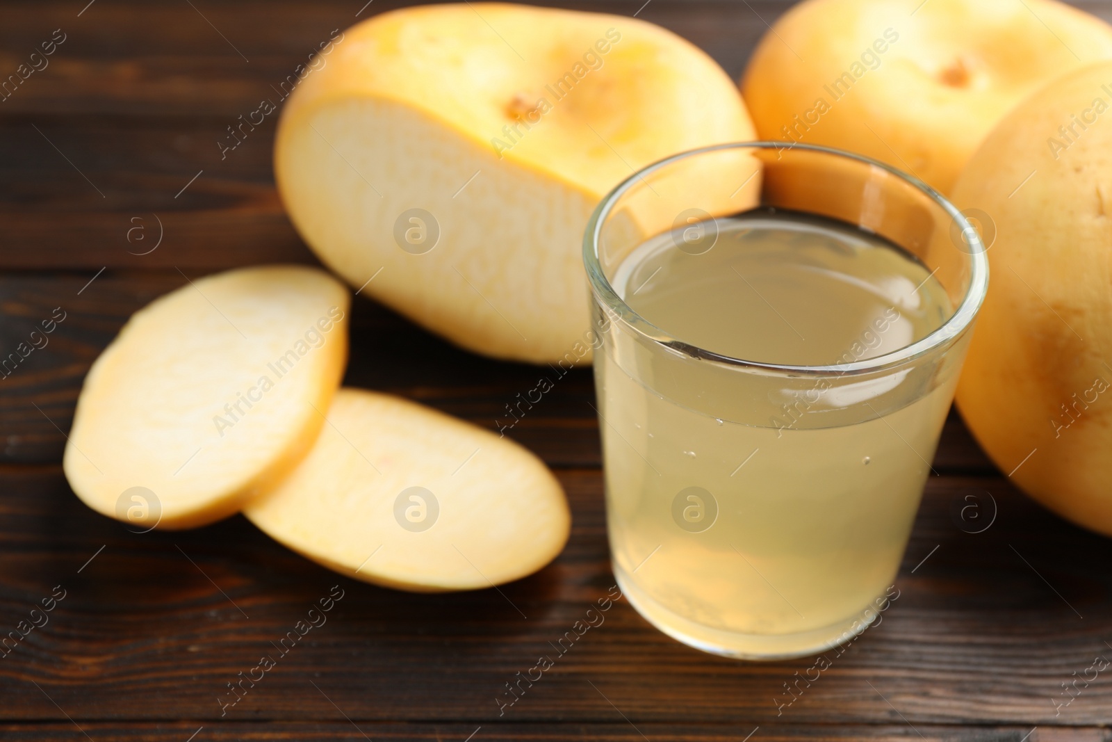 Photo of Glass of fresh natural turnip juice, cut and whole roots on wooden table, closeup. Space for text