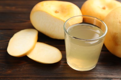 Photo of Glass of fresh natural turnip juice, cut and whole roots on wooden table, closeup. Space for text