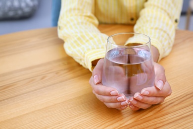 Photo of Woman holding glass of water at wooden table, closeup with space for text. Refreshing drink