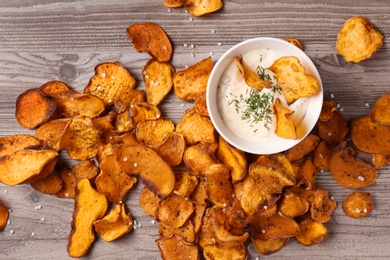 Photo of Sweet potato chips and bowl of sauce on wooden background, top view