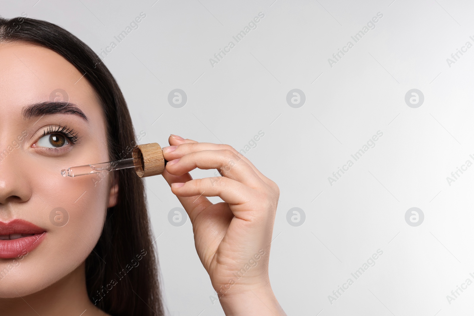 Photo of Young woman applying essential oil onto face on white background, closeup and space for text