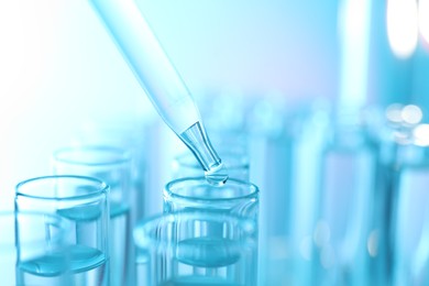 Photo of Dripping liquid from pipette into test tube on light blue background, closeup