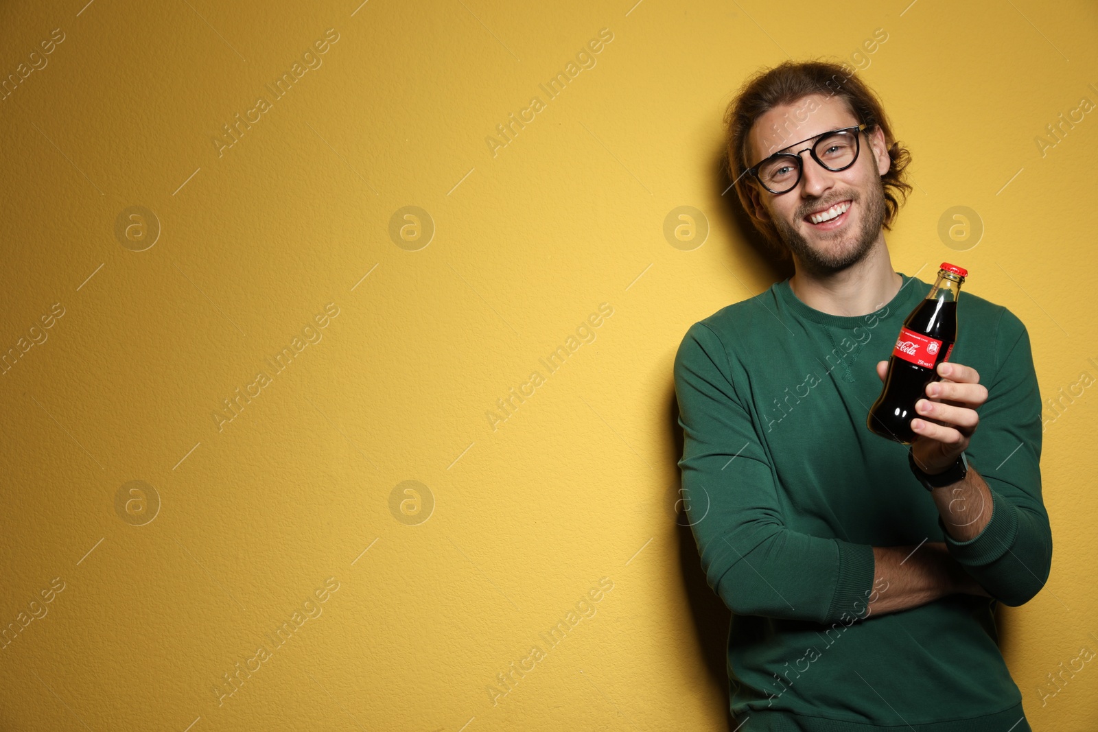 Photo of MYKOLAIV, UKRAINE - NOVEMBER 28, 2018: Young man with bottle of Coca-Cola on color background, space for text