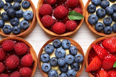 Tartlets with different fresh berries on white wooden table, flat lay. Delicious dessert