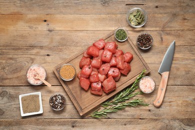 Photo of Cooking delicious goulash. Raw beef meat, knife and different spices on wooden table, flat lay