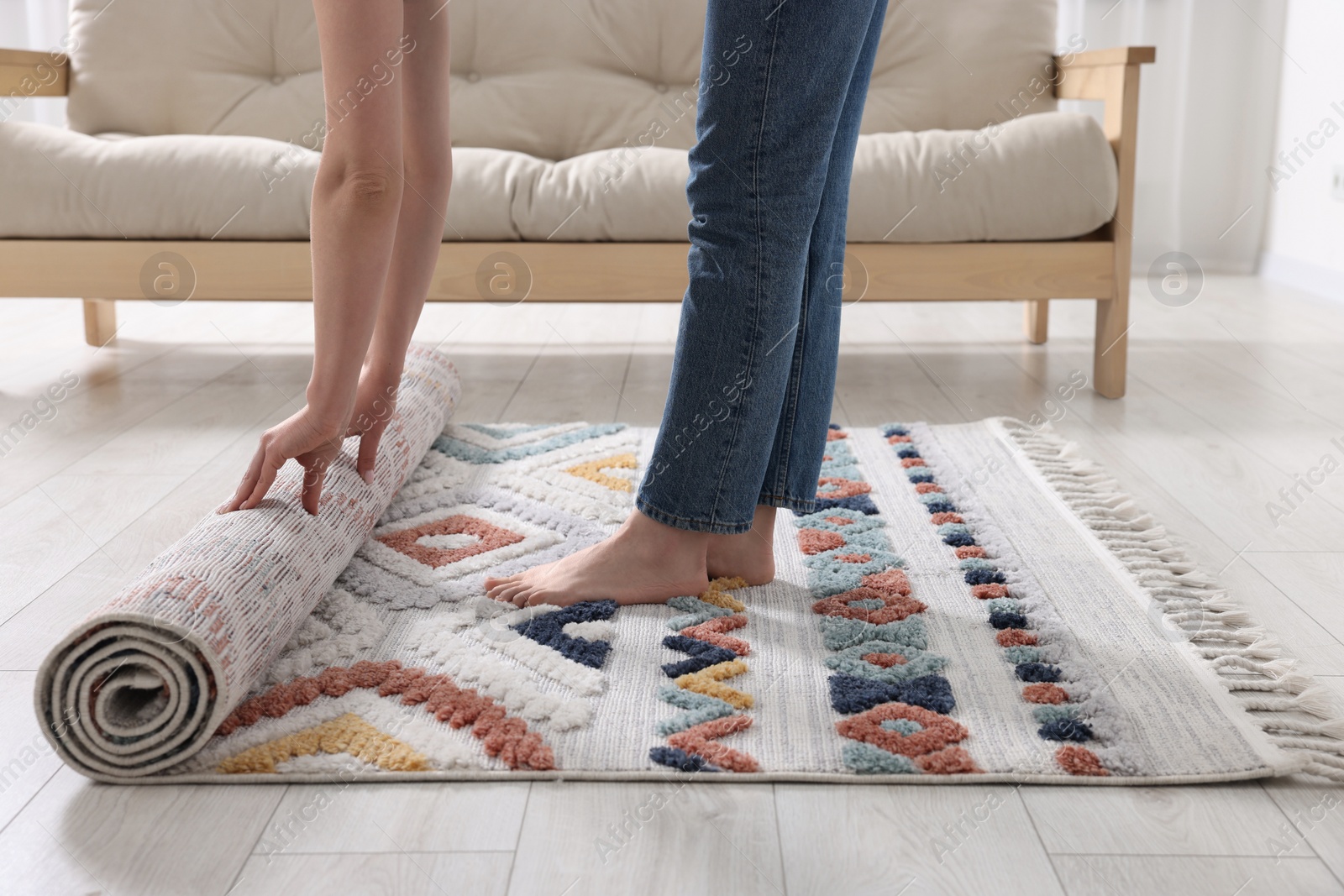 Photo of Woman unrolling carpet with beautiful pattern on floor in room, closeup