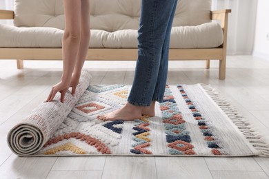 Woman unrolling carpet with beautiful pattern on floor in room, closeup