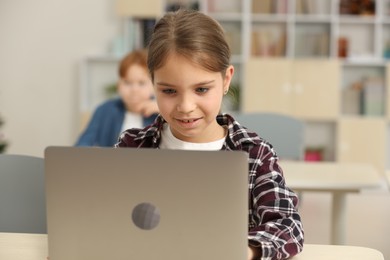 Photo of Smiling little girl with laptop studying in classroom at school