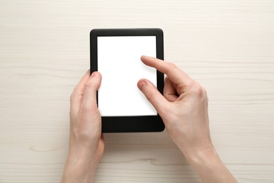 Photo of Woman using e-book reader at white wooden table, top view