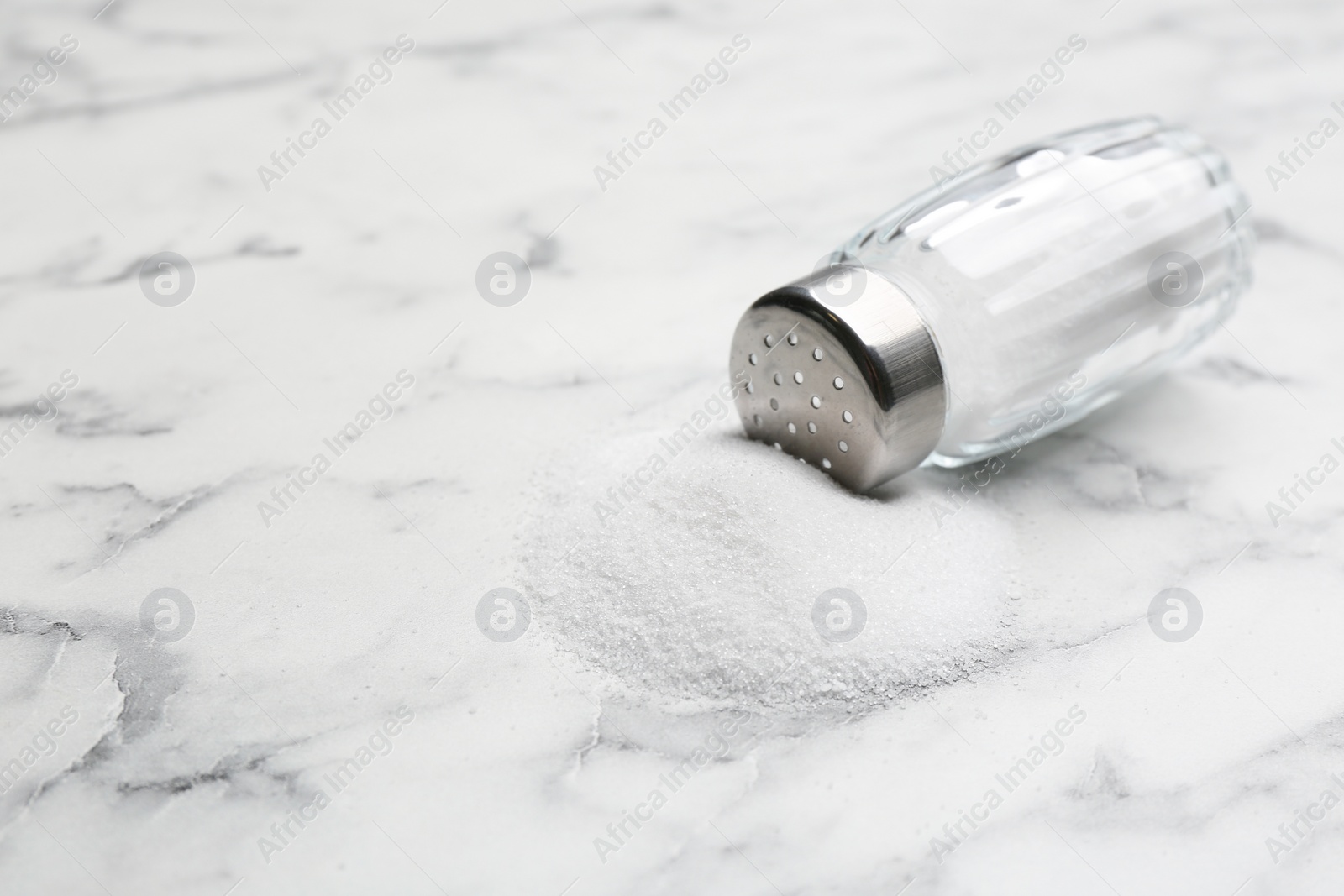 Photo of Scattered salt and shaker on white marble table, closeup. Space for text