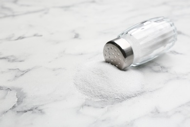 Photo of Scattered salt and shaker on white marble table, closeup. Space for text