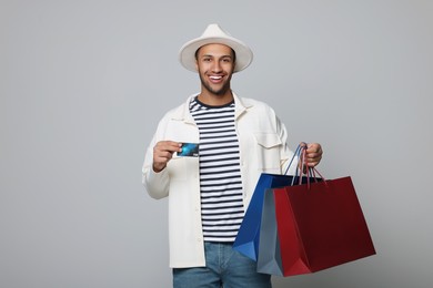Photo of Happy African American man in hat with shopping bags and credit card on light grey background