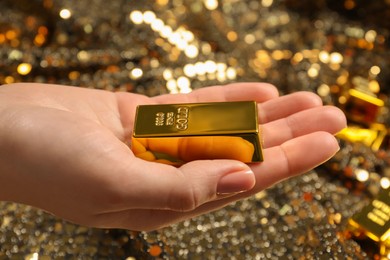 Woman holding shiny gold bar against sequin fabric, closeup