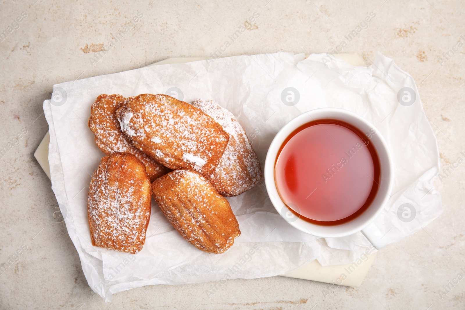 Photo of Delicious madeleine cakes with powdered sugar and tea on light grey table, top view