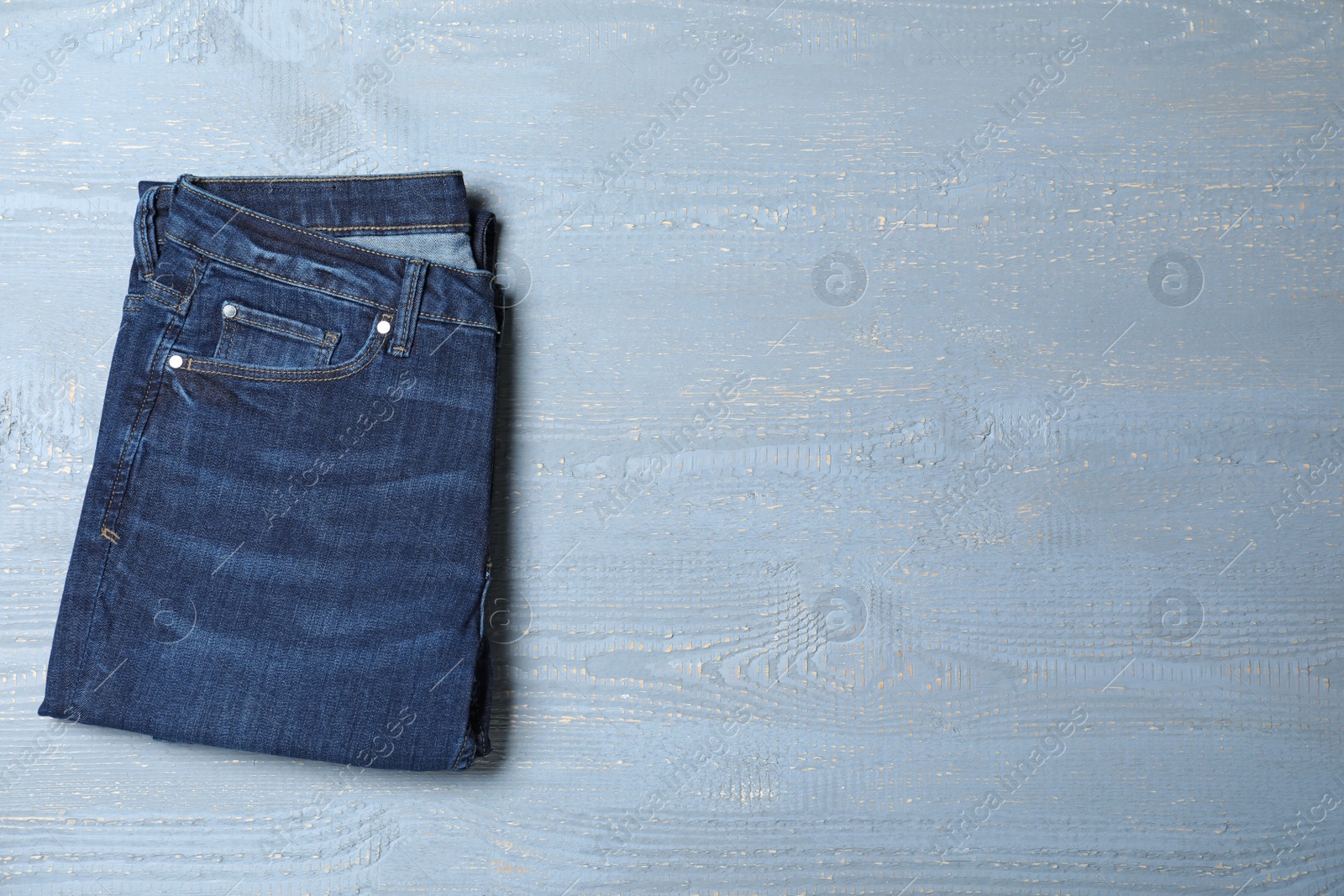 Photo of New stylish jeans on light grey wooden background, top view. Space for text