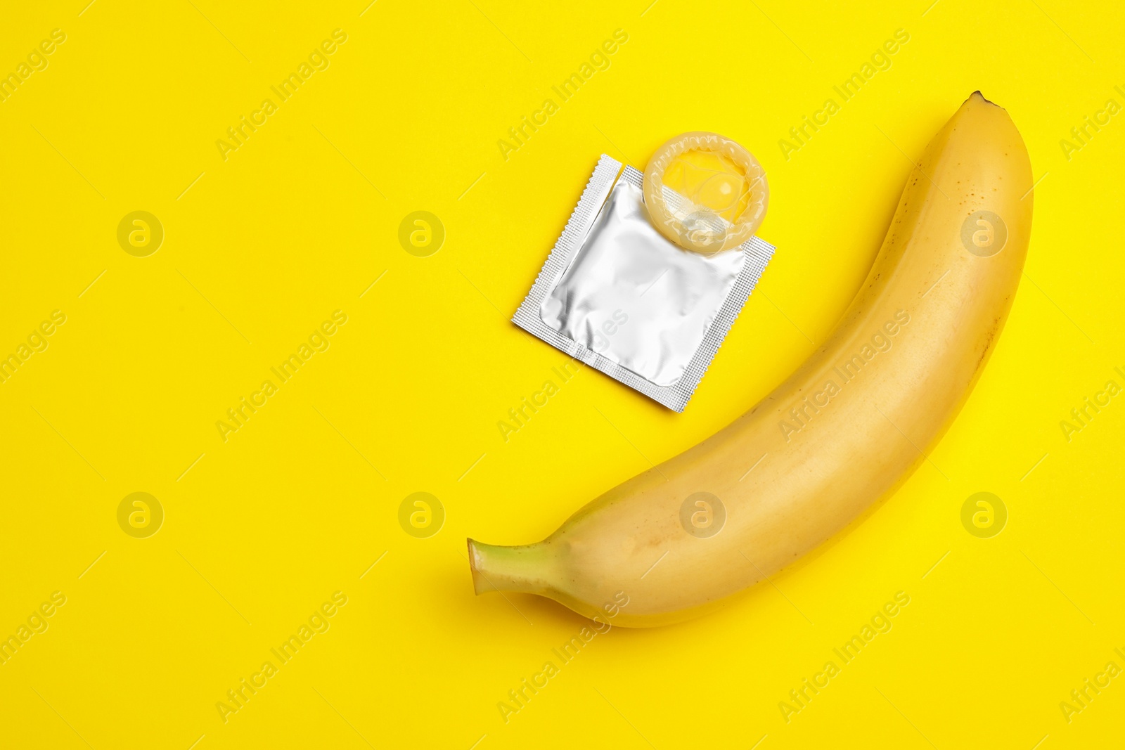 Photo of Condom with banana and space for text on yellow background, flat lay. Safe sex