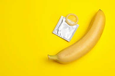 Condom with banana and space for text on yellow background, flat lay. Safe sex