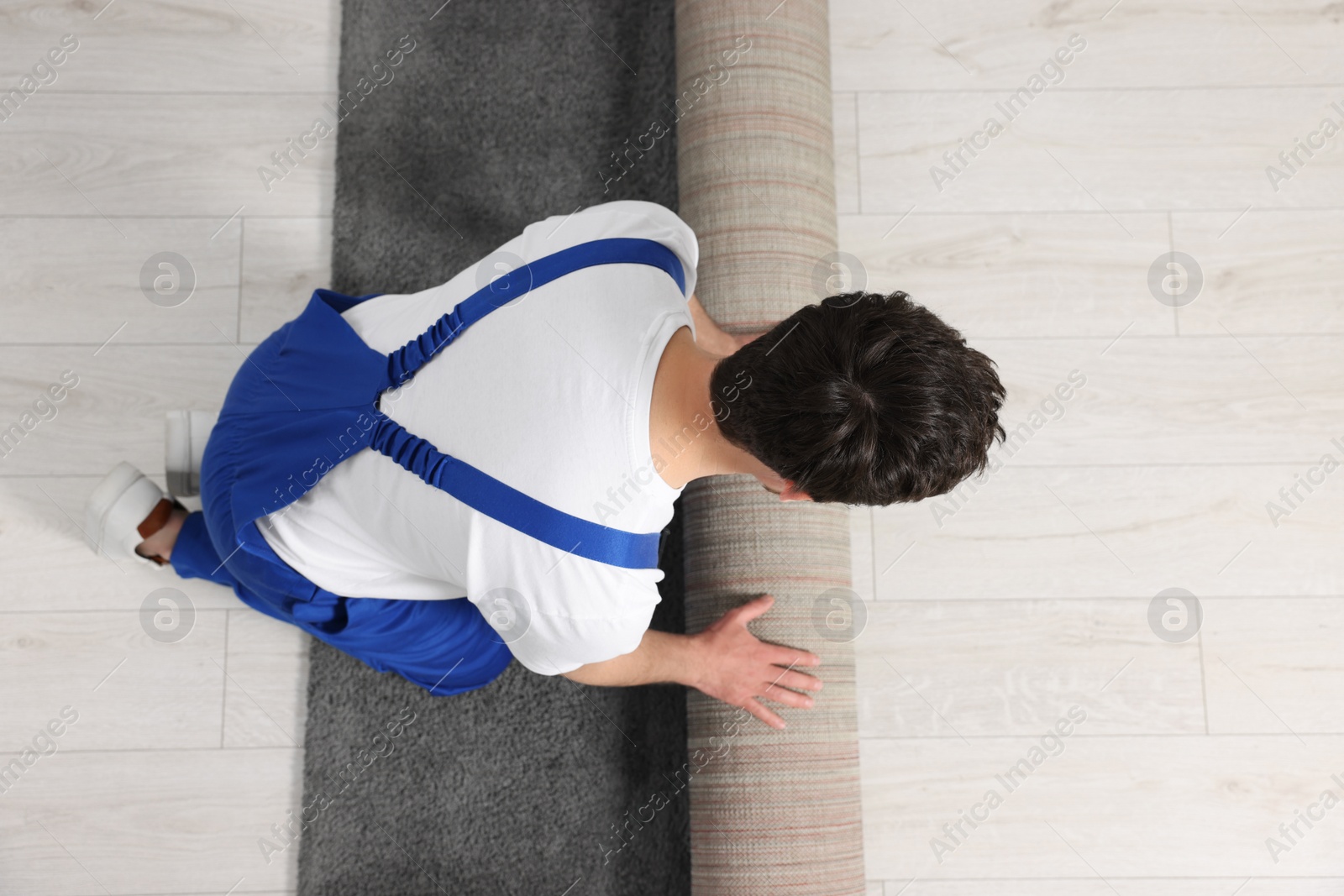 Photo of Worker unrolling new carpet in room, top view