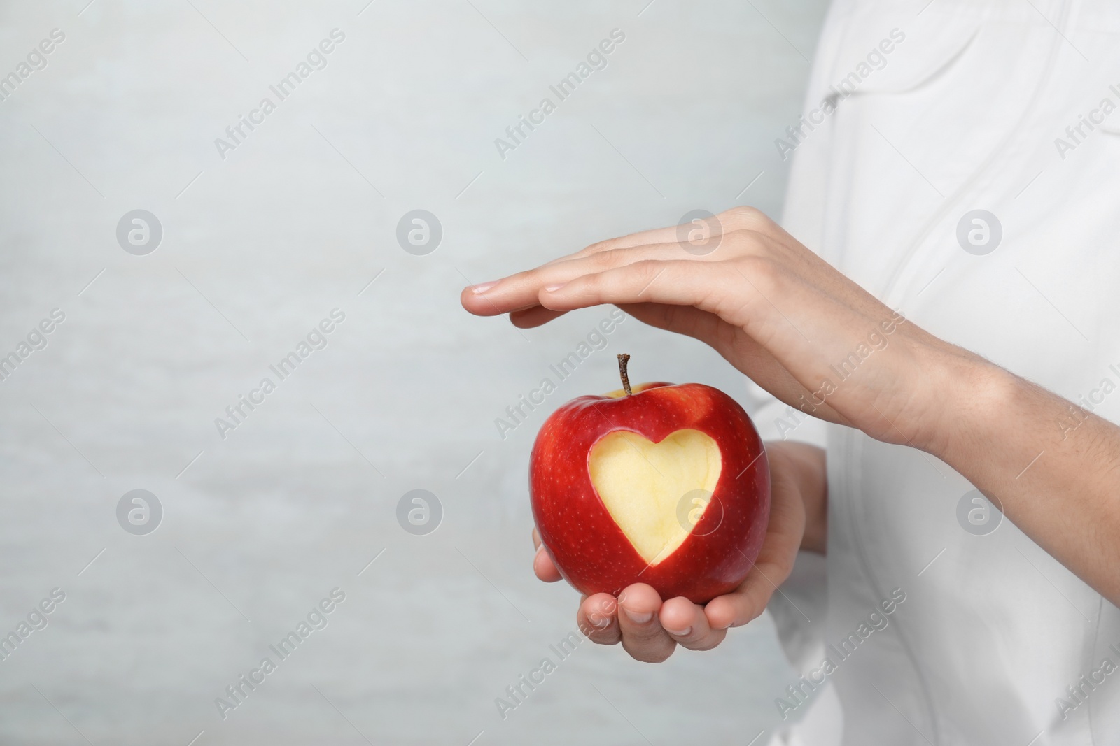 Photo of Woman holding apple with carved heart on light background, closeup. Space for text