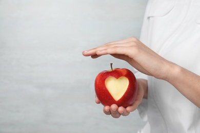 Photo of Woman holding apple with carved heart on light background, closeup. Space for text