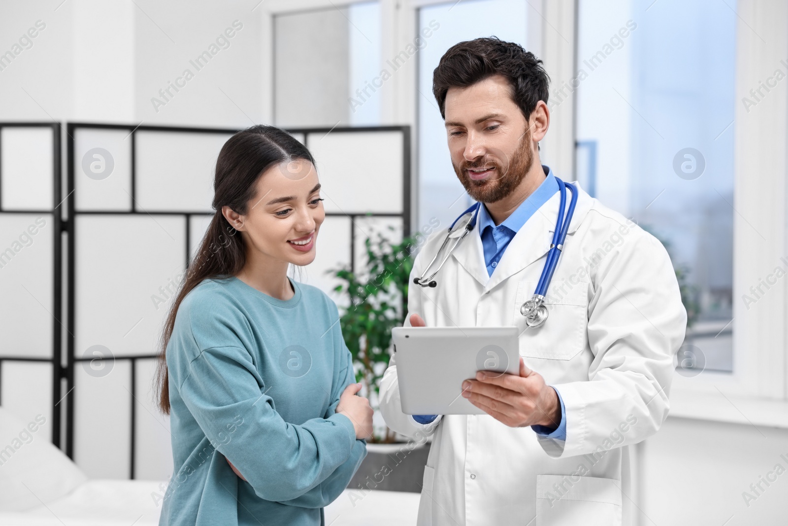 Photo of Doctor with tablet consulting patient during appointment in clinic