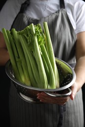 Woman holding colander with fresh green celery on black background, closeup