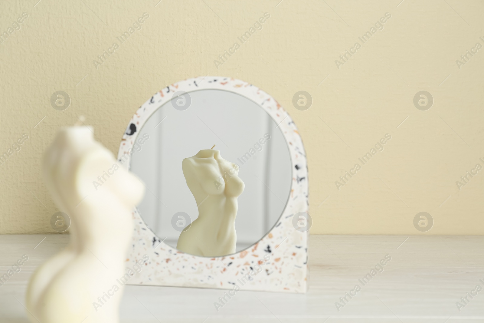 Photo of Beautiful female body shaped candle near mirror on white table