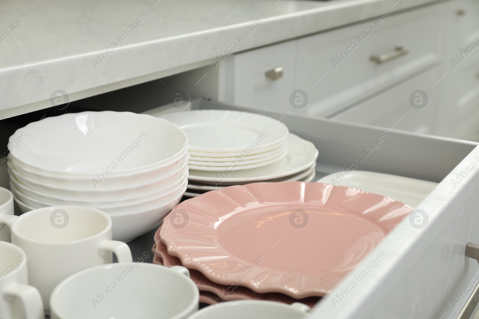 Photo of Clean plates, bowls and cups in drawer indoors, closeup