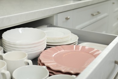 Photo of Clean plates, bowls and cups in drawer indoors, closeup