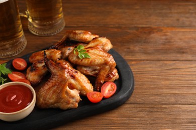 Photo of Mugs with beer, delicious baked chicken wings and sauce on wooden table. Space for text