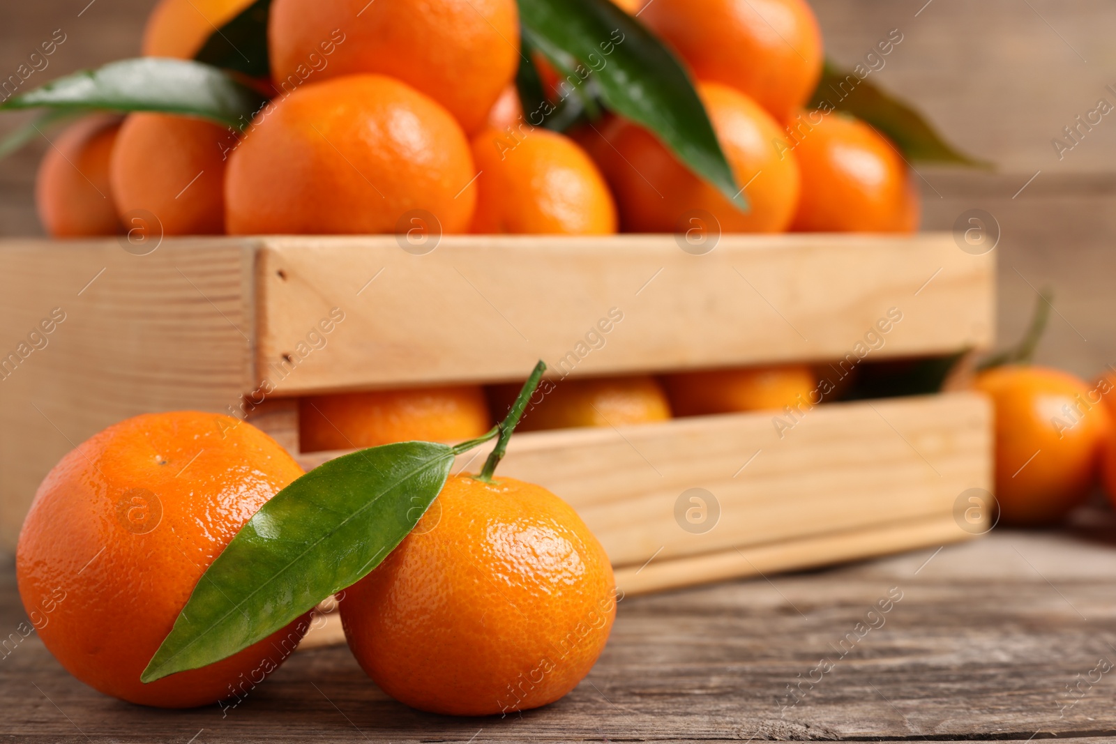 Photo of Delicious tangerines with leaves on wooden table, closeup