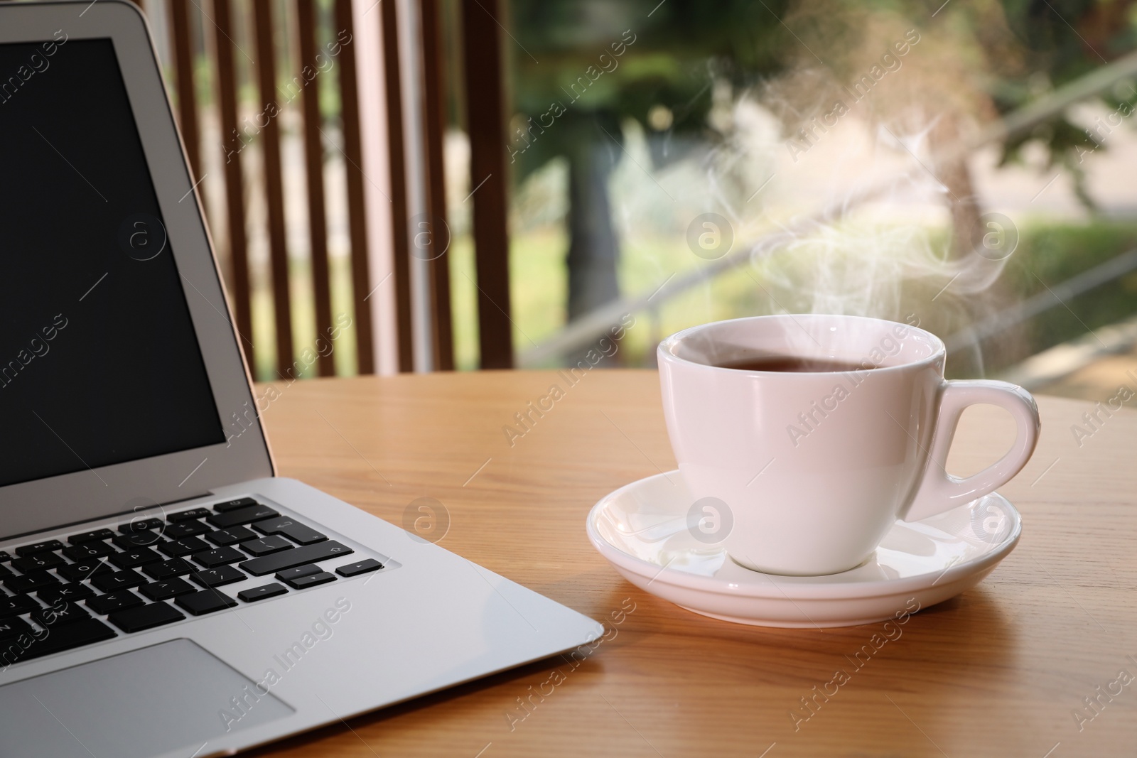 Photo of Cup of delicious morning coffee near laptop on wooden table
