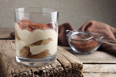 Photo of Delicious tiramisu in glass on wooden table, closeup. Space for text